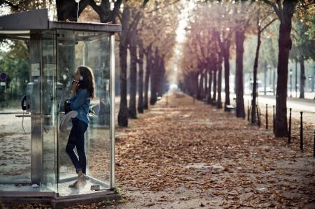 女孩在电话亭里，树木，散落着叶子，秋天在巴黎的大道